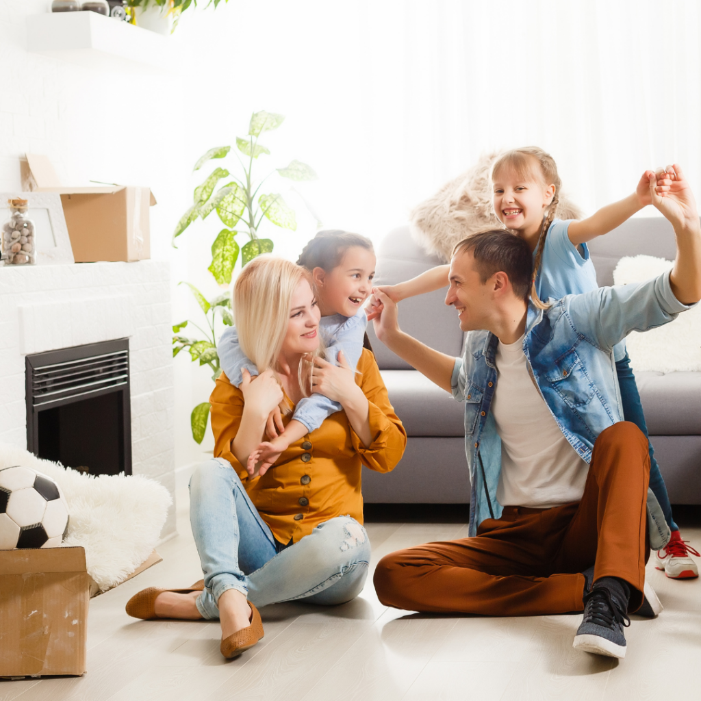 Famille heureuse en intérieur, préparant un déménagement: parents et deux filles jouent et célèbrent ensemble, près de cartons et ballons. Checklist déménagement intégrée.