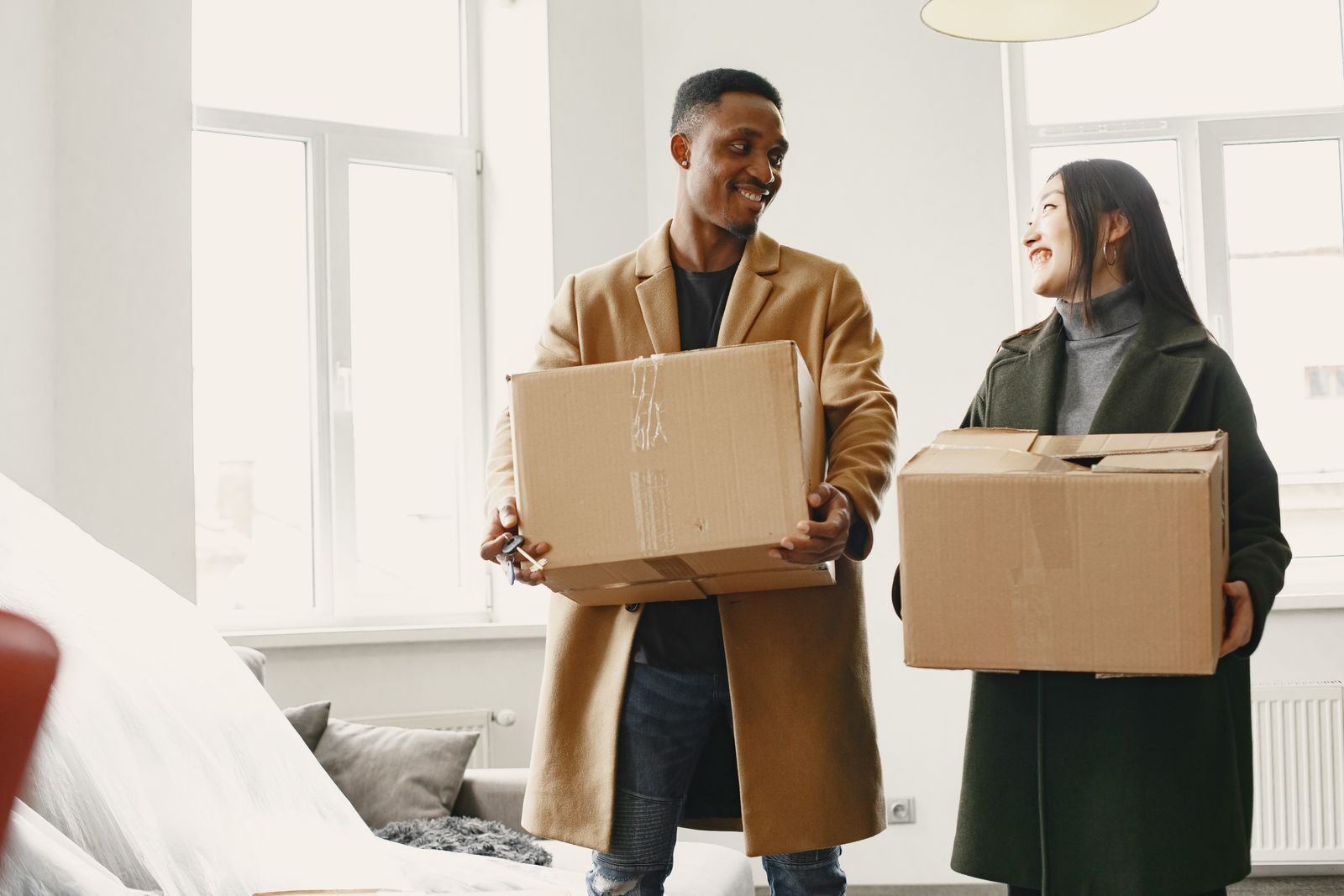 Deux personnes heureuses portent des cartons dans un intérieur lumineux, prêts à déménager.